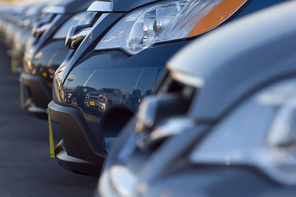 Row of brand new cars at a car dealership. Focus is on the headlight of a second car.